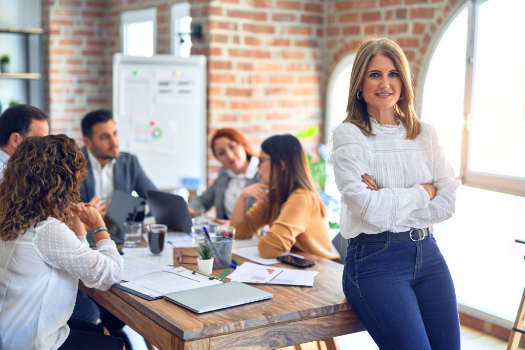 Team leader sitting on desk while members are discussing ideas